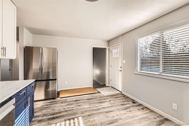 kitchen with stainless steel fridge, white cabinets, light stone counters, and light wood-type flooring