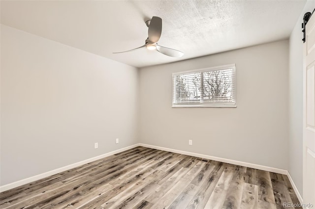 empty room featuring a barn door, ceiling fan, and hardwood / wood-style floors