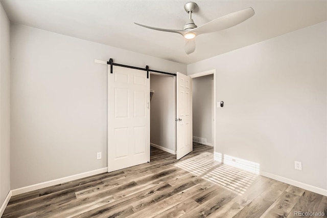 unfurnished bedroom featuring hardwood / wood-style flooring, ceiling fan, a barn door, and a closet