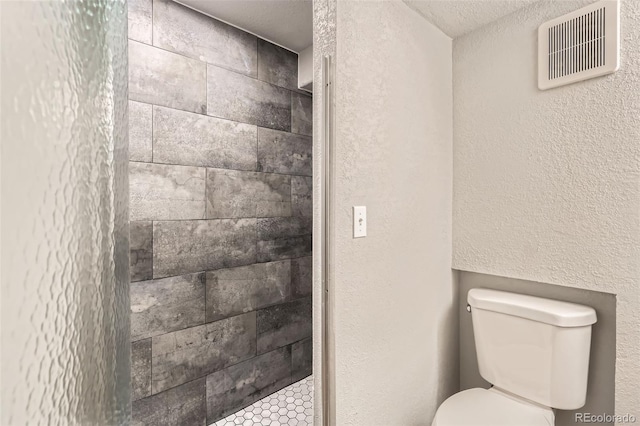 bathroom with tiled shower, toilet, and a textured ceiling