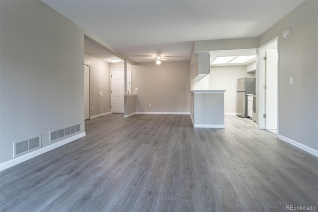 unfurnished living room featuring visible vents, baseboards, and wood finished floors