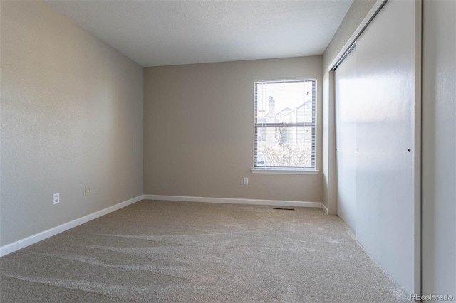 spare room featuring light colored carpet and baseboards