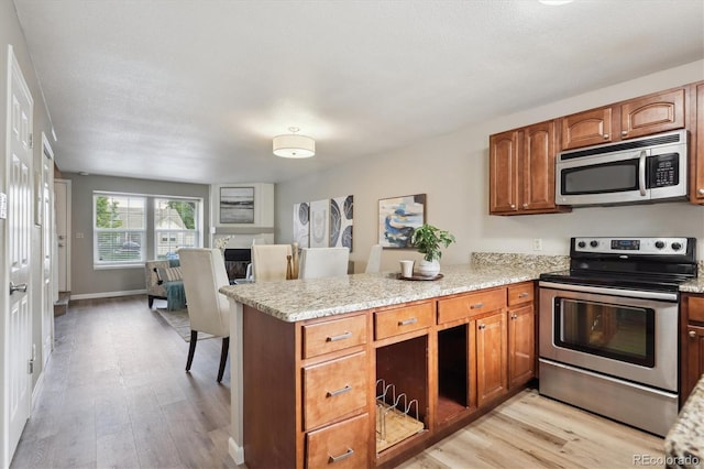 3078 W 107th Pl Unit D, Westminster, CO 80031 - kitchen featuring appliances with stainless steel finishes, a peninsula, light wood-style floors, and brown cabinetry