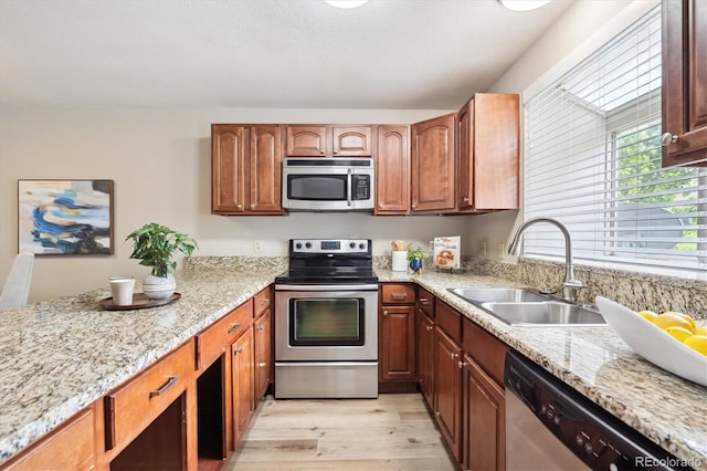 3078 W 107th Pl Unit D, Westminster, CO 80031 - kitchen featuring stainless steel appliances, light wood-style flooring, light stone counters, a peninsula, and brown cabinetry