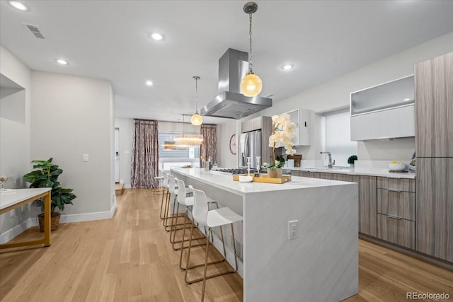 kitchen featuring island range hood, white cabinets, hanging light fixtures, light hardwood / wood-style floors, and a center island with sink