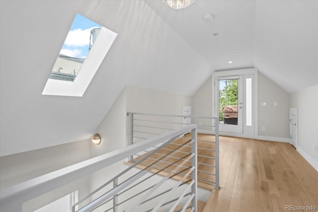 corridor with lofted ceiling with skylight and light hardwood / wood-style floors