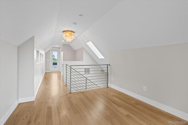 bonus room featuring lofted ceiling with skylight, light hardwood / wood-style floors, and a chandelier