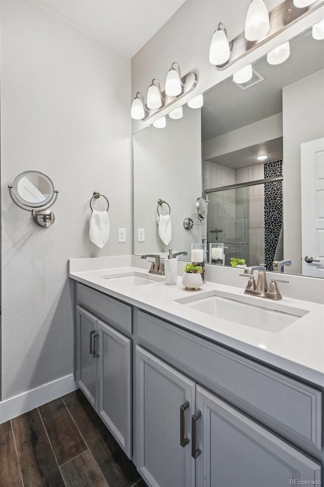 full bath with double vanity, wood finished floors, a shower stall, and a sink