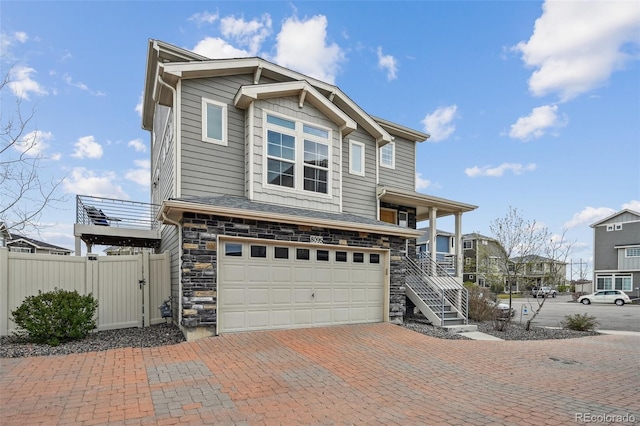 view of front of house featuring an attached garage, stone siding, fence, decorative driveway, and stairway