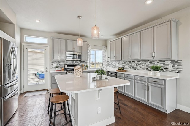 kitchen featuring gray cabinets, stainless steel appliances, tasteful backsplash, and a breakfast bar