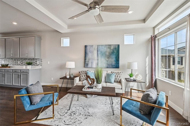 living room featuring a ceiling fan, baseboards, a tray ceiling, and plenty of natural light