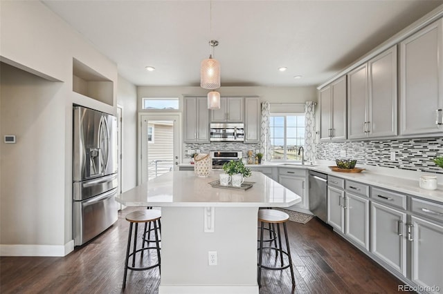 kitchen with a sink, gray cabinetry, a breakfast bar area, and appliances with stainless steel finishes
