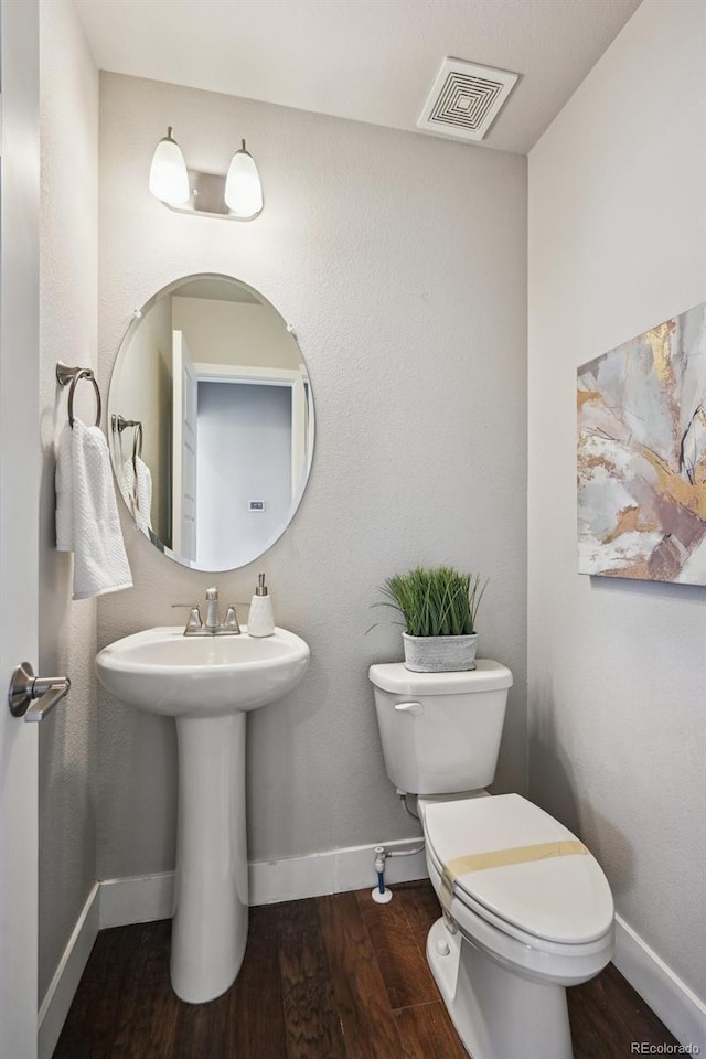 half bath with toilet, baseboards, visible vents, and wood finished floors