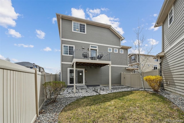 rear view of house featuring a balcony, a patio area, a fenced backyard, and a lawn