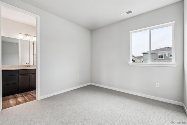 unfurnished bedroom featuring visible vents, connected bathroom, baseboards, carpet, and a sink