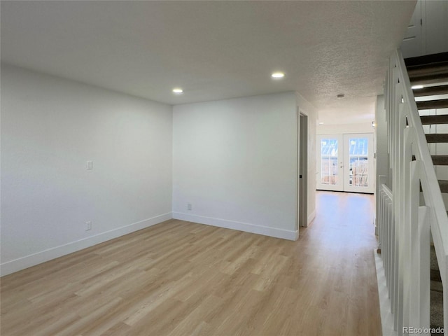 empty room with a textured ceiling, french doors, and light wood-type flooring