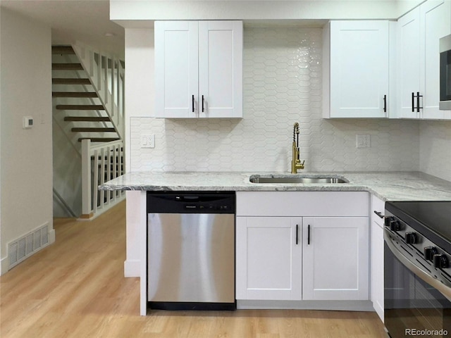 kitchen with appliances with stainless steel finishes, decorative backsplash, sink, white cabinets, and light stone counters