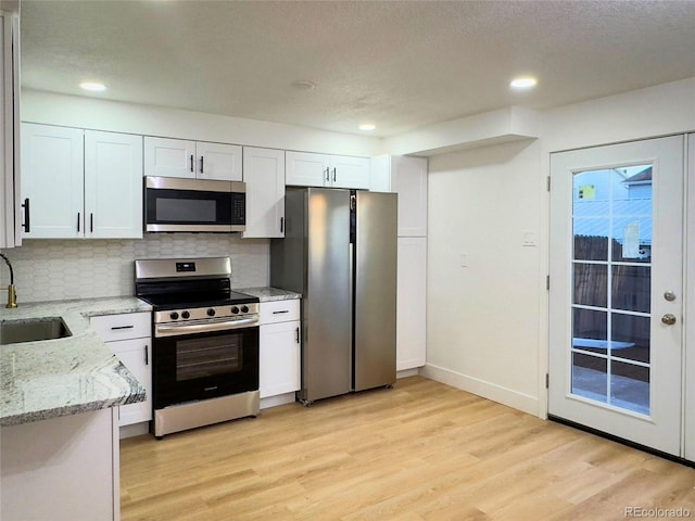 kitchen featuring appliances with stainless steel finishes, sink, white cabinets, backsplash, and light stone counters