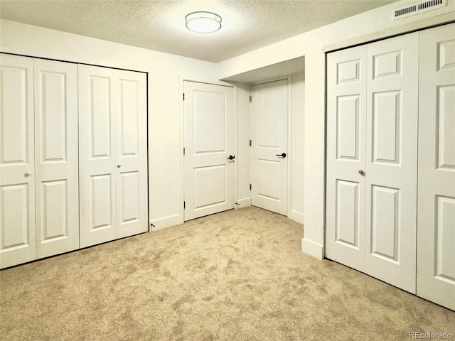 unfurnished bedroom featuring light colored carpet, a textured ceiling, and two closets