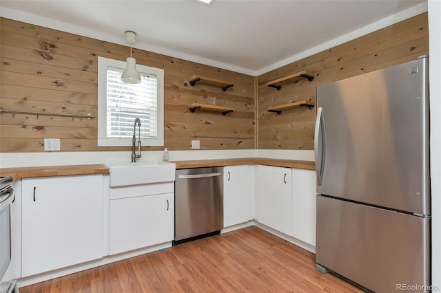 kitchen with white cabinets, appliances with stainless steel finishes, light countertops, light wood-type flooring, and a sink