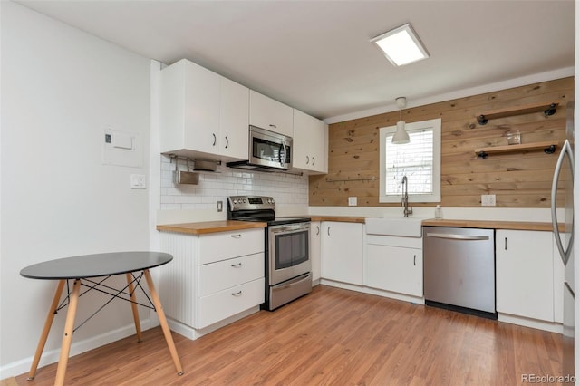 kitchen with light wood finished floors, appliances with stainless steel finishes, decorative backsplash, and white cabinets