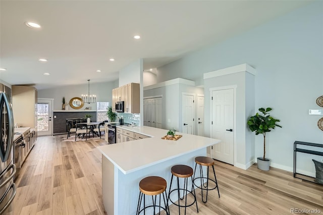 kitchen featuring a kitchen breakfast bar, appliances with stainless steel finishes, light hardwood / wood-style floors, pendant lighting, and decorative backsplash