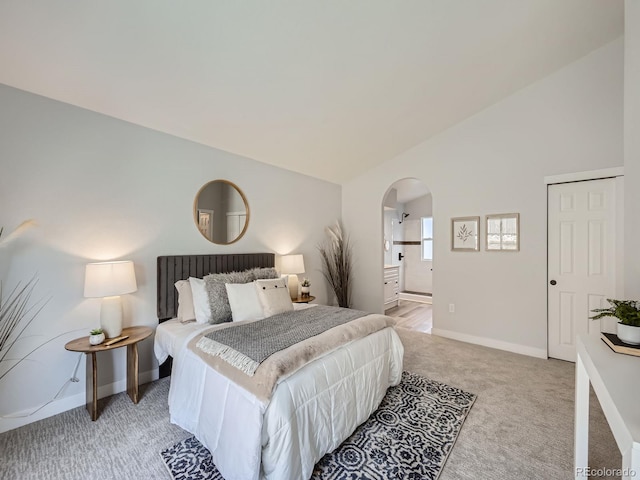 bedroom with lofted ceiling, ensuite bath, and light colored carpet