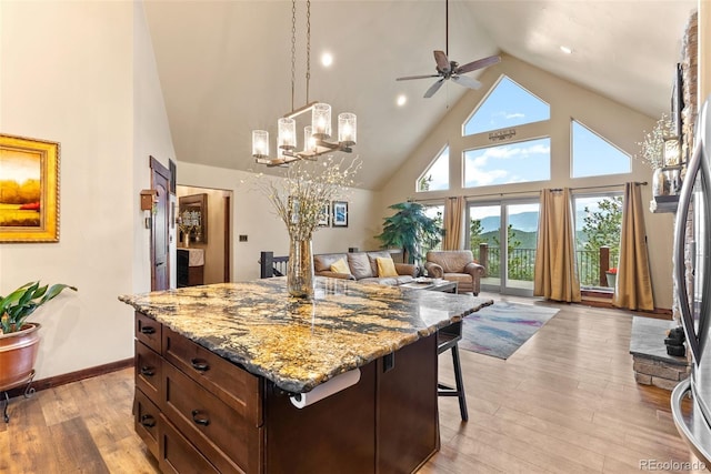 kitchen with a breakfast bar area, a ceiling fan, light wood-type flooring, high vaulted ceiling, and open floor plan