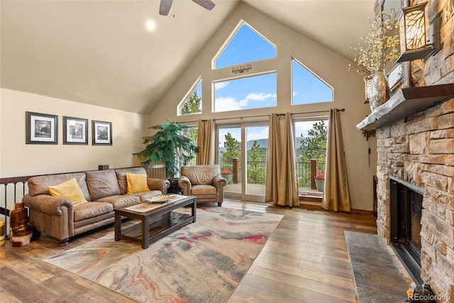 living room featuring a ceiling fan, high vaulted ceiling, a stone fireplace, and hardwood / wood-style floors