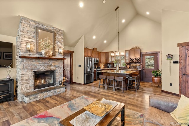 living area with a stone fireplace, wood finished floors, high vaulted ceiling, baseboards, and recessed lighting