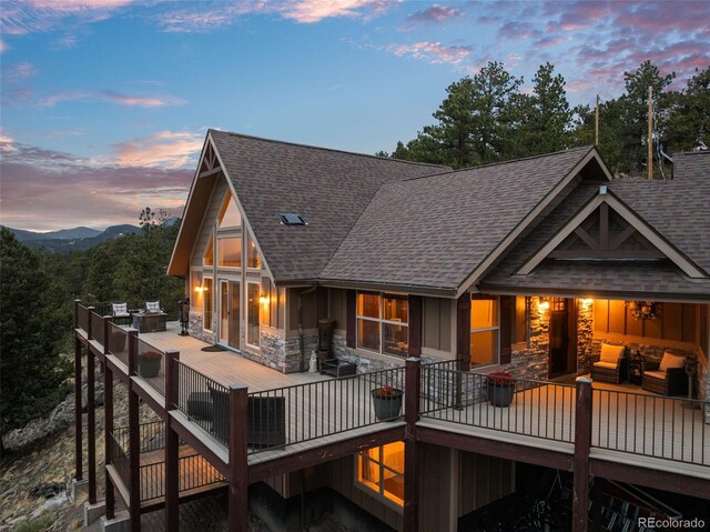 854 Dick Mountain Dr, Bailey, CO 80421 - back of house at dusk with stone siding, roof with shingles, and board and batten siding