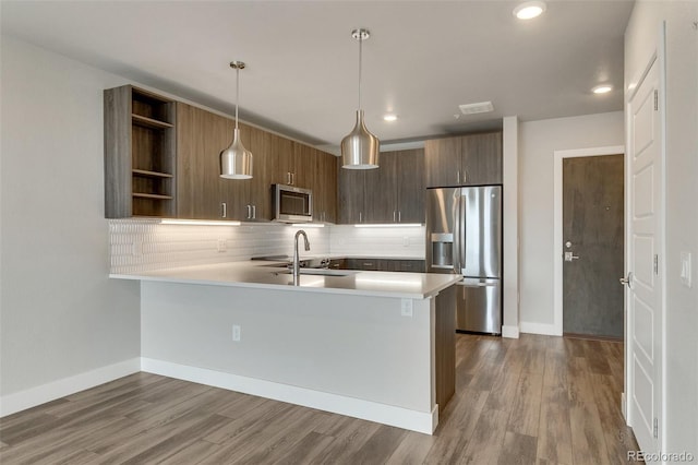 kitchen with appliances with stainless steel finishes, decorative light fixtures, wood-type flooring, sink, and kitchen peninsula