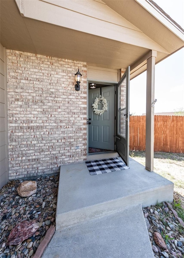 doorway to property featuring fence and brick siding