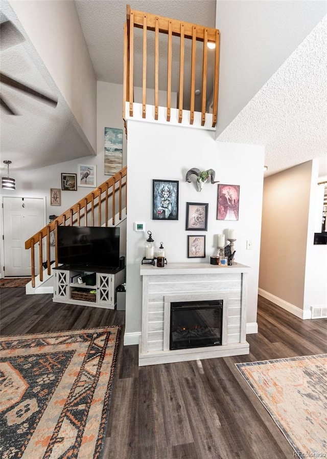 living room featuring visible vents, a glass covered fireplace, wood finished floors, stairway, and a textured ceiling