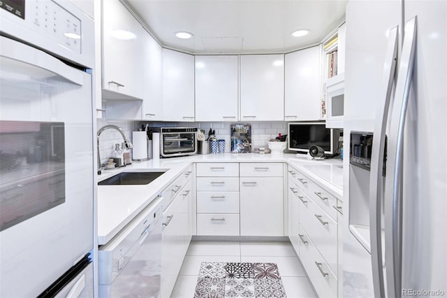 kitchen with sink, white appliances, light tile patterned floors, and white cabinets