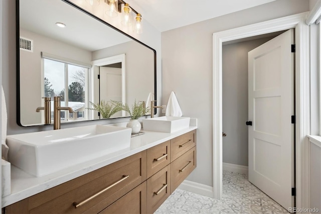 bathroom with double vanity, baseboards, visible vents, and a sink