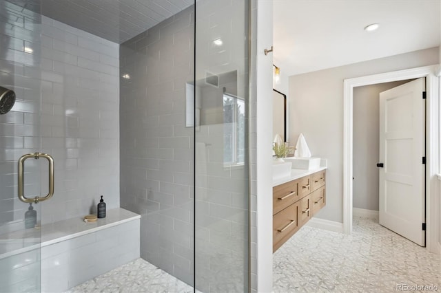 bathroom featuring a tile shower, vanity, and baseboards