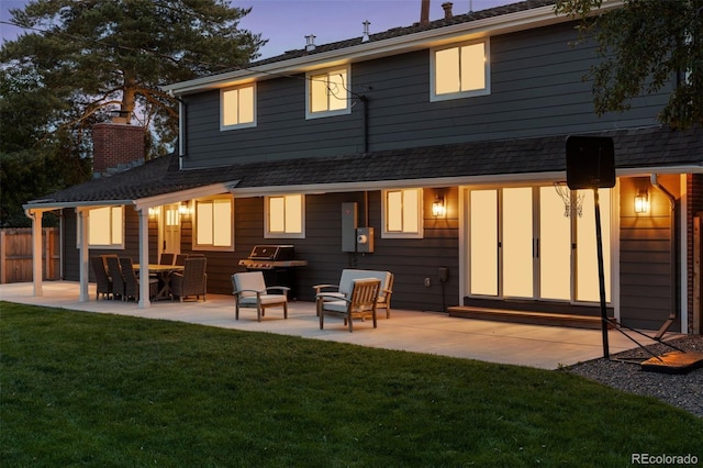 back of house at dusk featuring entry steps, a yard, a patio area, and fence