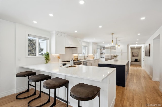 kitchen with custom range hood, a kitchen island, decorative light fixtures, a peninsula, and light countertops