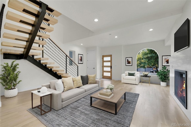 living area featuring light wood-type flooring, recessed lighting, stairs, and a glass covered fireplace