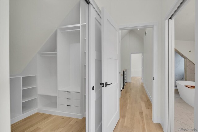 corridor with built in shelves, light hardwood / wood-style floors, and vaulted ceiling