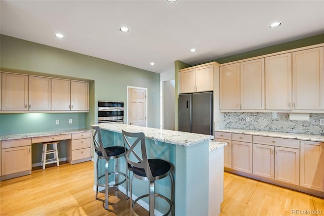 kitchen with light stone countertops, light brown cabinetry, a breakfast bar, light hardwood / wood-style floors, and stainless steel refrigerator