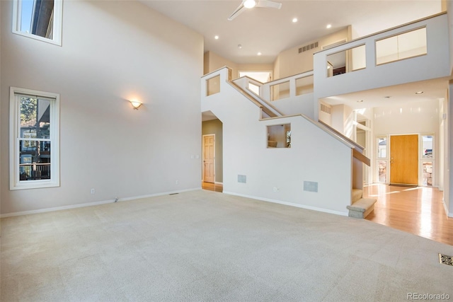 unfurnished living room featuring light carpet, a towering ceiling, and ceiling fan