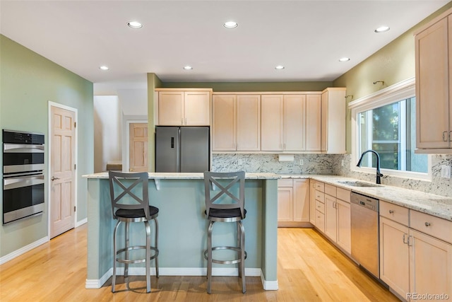 kitchen with sink, light stone counters, a breakfast bar area, light brown cabinetry, and appliances with stainless steel finishes