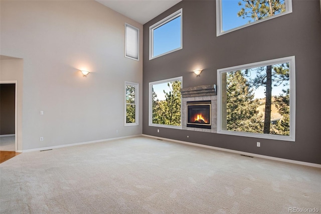 unfurnished living room featuring a fireplace, light carpet, and a towering ceiling