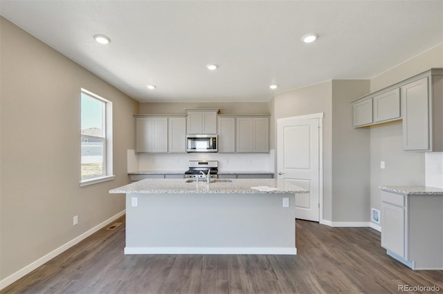 9910 Biscay St, Commerce City, CO 80022 - kitchen with appliances with stainless steel finishes, a center island with sink, dark wood-style flooring, light stone counters, and recessed lighting