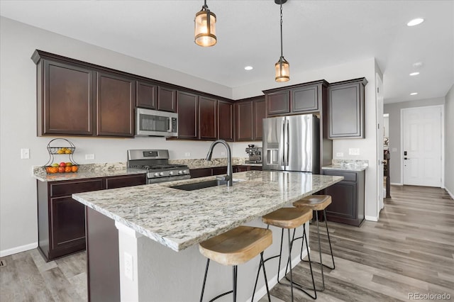 kitchen featuring pendant lighting, a center island with sink, sink, light hardwood / wood-style floors, and stainless steel appliances