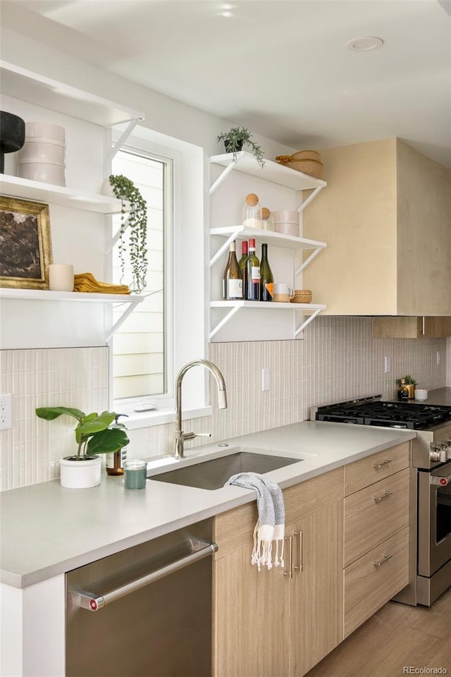 kitchen featuring stainless steel appliances, light brown cabinetry, open shelves, a sink, and backsplash