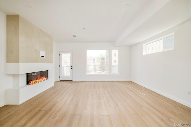 unfurnished living room with light wood-style flooring, a glass covered fireplace, and baseboards