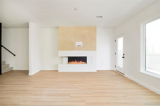 unfurnished living room featuring stairs, light wood-type flooring, a large fireplace, and baseboards